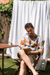 © nomad studio/Stocksy - Man reading a book sitting on chair outdoors.