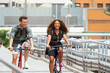 © David Prado/Stocksy - Happy diverse couple riding bikes on bridge