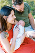 © Serena Burroughs/Stocksy - smiling mother and father sitting outside with newborn baby in arms