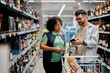 © Drazen - Young man using smart phone and talking to female worker while shopping in supermarket.