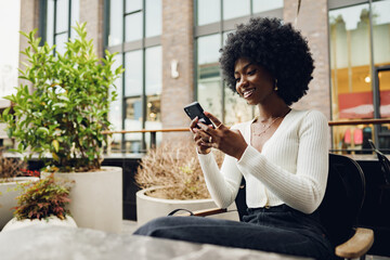 Wall Mural - Portrait of a beautiful young african woman using her cellphone in a cafe