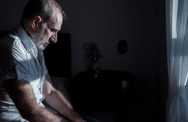 Portrait of adult man sitting on bed with sunlight and shadow