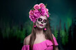 Young woman with painted skull on her face for Mexico's Day of the Dead against dark green background