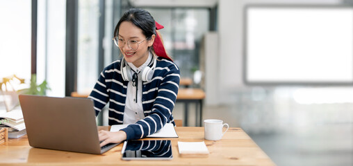 Fototapete - Shot of young asian female student sitting at table and using laptop computer. Young female student studying in library.