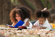 Happy two African American child girl laying and writing on a book outdoors in the park. Kids girl learning outside at the school