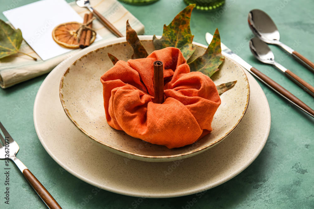 Stylish dinnerware and pumpkin made of napkin on green table, closeup
