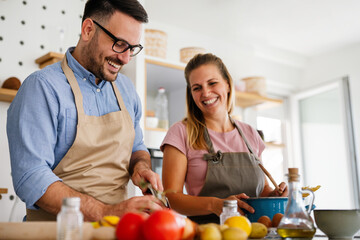 Wall Mural - Young happy couple is enjoying and preparing healthy meal in their kitchen together