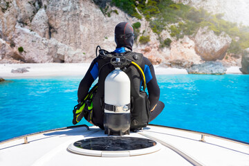 Wall Mural - A scuba diver with his equipment sits on a bow of a boat in front of a beautiful beach with turquoise sea