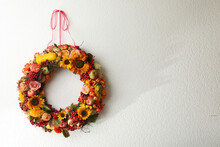 Beautiful Autumnal Wreath With Flowers, Berries And Fruits Hanging On White Wall. Space For Text