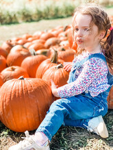 Young Girl Sitting In Pumpkin Patch