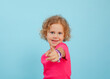 © Татьяна Волкова - Portrait of blue-eyed little girl with curly fair hair looking, pointing at camera with index finger on blue background.
