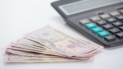 Wall Mural - dollar banknotes near blurred calculator on white background.