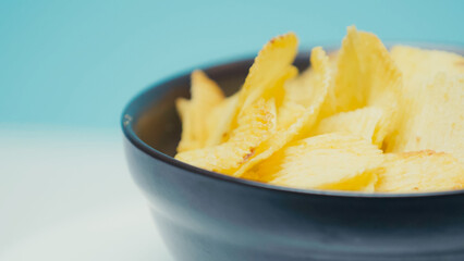 Sticker - close up view of crunchy and ridged potato chips in bowl on blue with copy space.