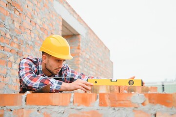 Using bricks. Young construction worker in uniform is busy at the unfinished building