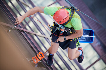 Wall Mural - Industrial mountaineering worker washing glass windows of high-rise building, hanging on safety climbing rope. Man window cleaner in protective helmet cleaning skyscraper facade. Top view.