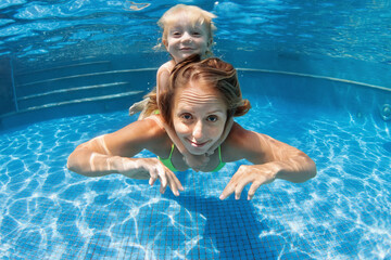 Wall Mural - Happy family - young mother, baby boy learn to swim, dive underwater. Jump with fun in swimming pool. Healthy lifestyle, active parents, people water sports activities on summer holidays with kids.