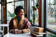 © Drazen - Happy black woman looks through window while enjoying in cup of warm tea in cafe during winter season.
