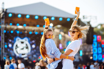 Wall Mural - Two female friends drink beer and have fun at the music festival.  Summer holiday, vacation concept.