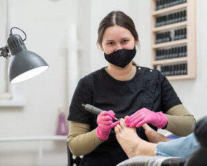 The pedicure master processes the client's foot using an apparatus with an abrasive disc.