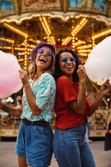 Young multiracial women eating cotton candy in attraction park