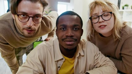 Caucasian woman, African American and European man discusses something and looks at the camera as if in a monitor in an office for the development of games and computer applications.