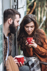 Wall Mural - Young beautiful loving couple travelling across country in the van. Millennial man and woman in a travel camper. Cozy atmosphere, vacations vibe. Drinking tea, cooking marshmallow on a campfire