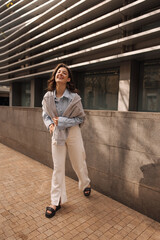 Wall Mural - Full length happy young caucasian girl spending time outdoors during break from work. Brunette wears shirt, pants and sweatshirt. Good mood concept