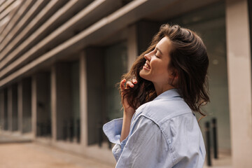 Wall Mural - Relaxed young caucasian woman smiling with her eyes closed resting after work near office. Brunette manager wears blue shirt. People sincere emotions lifestyle concept.