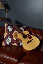 Acoustic Guitar On Rich Brown Leather Sofa. Colorful Pillow With Geometric Southwest Design. Closeup Copyspace. 