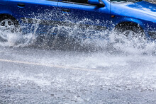 Rain Water Splashing From Wheels Of Blue Car In Motion. Rainy Weather.