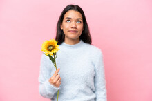 Young Colombian Woman Holding Sunflower Isolated On Pink Background And Looking Up