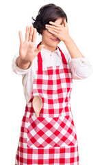 Sticker - Beautiful young woman with short hair wearing professional cook apron covering eyes with hands and doing stop gesture with sad and fear expression. embarrassed and negative concept.