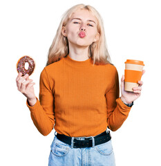 Wall Mural - Young caucasian woman eating doughnut and drinking coffee looking at the camera blowing a kiss being lovely and sexy. love expression.