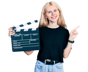 Sticker - Young caucasian woman holding video film clapboard smiling happy pointing with hand and finger to the side