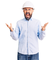 Canvas Print - Young handsome man wearing architect hardhat crazy and mad shouting and yelling with aggressive expression and arms raised. frustration concept.