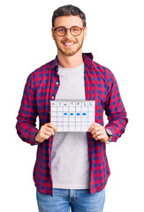 Wall Mural - Handsome young man with bear holding travel calendar looking positive and happy standing and smiling with a confident smile showing teeth