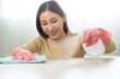 Happy cleanliness, asian young woman working chore cleaning on table, hand wearing glove using rag rub remove dust with spray bottle. Household hygiene clean up, cleaner, equipment tool for cleaning