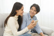 Happy couple love at home,beautiful two asian young spending good time together,bonding to each other and smiling romantic on sofa in living room while man embrace woman using smartphone, mobile phone