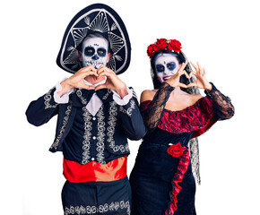 Poster - Young couple wearing mexican day of the dead costume over background smiling in love doing heart symbol shape with hands. romantic concept.