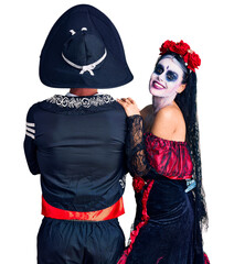 Poster - Young couple wearing mexican day of the dead costume over background standing backwards looking away with crossed arms