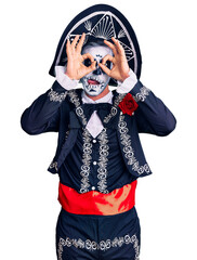 Canvas Print - Young man wearing day of the dead costume over background doing ok gesture like binoculars sticking tongue out, eyes looking through fingers. crazy expression.