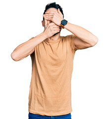 Poster - Hispanic man with beard wearing casual t shirt covering eyes and mouth with hands, surprised and shocked. hiding emotion