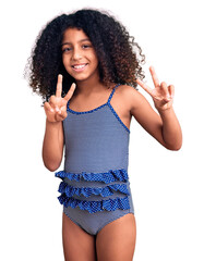 African american child with curly hair wearing swimwear smiling looking to the camera showing fingers doing victory sign. number two.