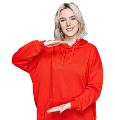 Poster - Young blonde girl wearing casual clothes gesturing with hands showing big and large size sign, measure symbol. smiling looking at the camera. measuring concept.