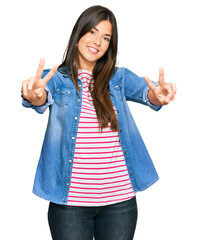 Poster - Young brunette woman wearing casual clothes smiling with tongue out showing fingers of both hands doing victory sign. number two.