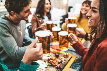 Happy friends enjoying happy hour drinking beer at brewery pub - Group of young people hanging out dining together at bar restaurant - Beverage lifestyle and friendship concept