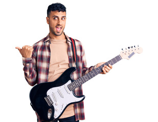 Poster - Young hispanic man playing electric guitar pointing thumb up to the side smiling happy with open mouth