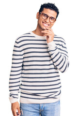 Sticker - Hispanic handsome young man wearing casual clothes and glasses looking confident at the camera with smile with crossed arms and hand raised on chin. thinking positive.