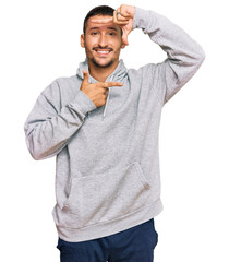 Canvas Print - Handsome man with tattoos wearing casual sweatshirt smiling making frame with hands and fingers with happy face. creativity and photography concept.