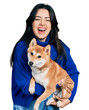 Beautiful hispanic woman holding cute dog smiling and laughing hard out loud because funny crazy joke.